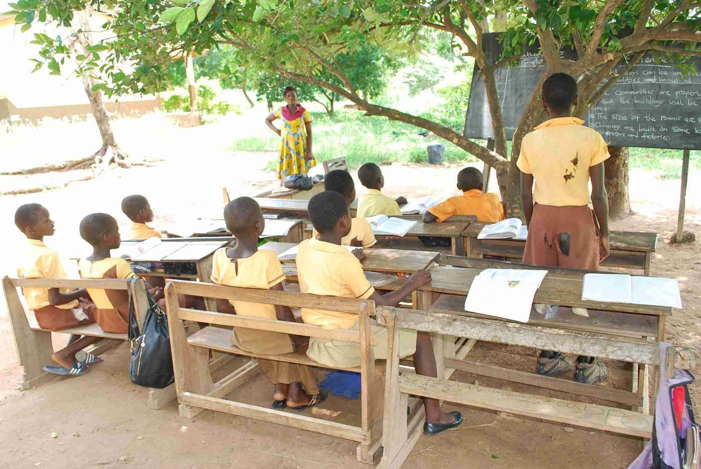 Pupils taking a lesson outdoors under a tree, a reminder of why local schools need proper classrooms